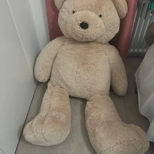 Teddybjörn 140cm - Stor och gosig nallebjörn i ljusbrun färg. Perfekt för kramar och som en mysig inredningsdetalj i sovrummet eller vardagsrummet. Den har en söt, rund nos och stora tassar. Passar både barn och vuxna som älskar mjuka leksaker. 140cm