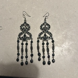 Eleganta silverfärgade örhängen med svarta pärlor - Säljer ett par eleganta örhängen i silverfärg med vackra svarta pärlor. De har en unik design med hängande detaljer som ger en lyxig känsla. Perfekta för festliga tillfällen eller när du vill känna dig extra glamorös. Passar till både vardag och fest!