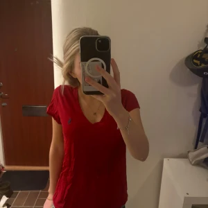 Röd t-shirt från Ralph Lauren - Säljer en snygg röd t-shirt från Ralph Lauren med en klassisk v-ringning. Den har en liten blå logga på bröstet och är i ett mjukt bomullsmaterial. Perfekt för vardagsbruk eller en avslappnad dag ute. Passar bra till jeans eller shorts!