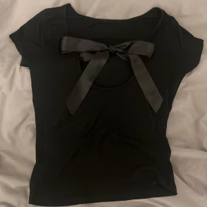 Svart t-shirt med urringad rygg och rosett i siden - Så fin och elegant T-shirt som passar perfekt till alla tillfällen, både uppklädda och vardagliga 