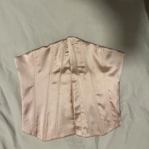 Rosa korsett - Snygg beige korsett i sidenmaterial från zara. Perfekt för fest eller en stilren look. Den har en tight passform och ger en elegant siluett. Passar bra till både kjol och byxor.