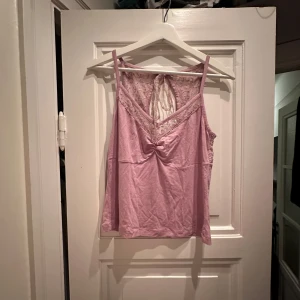 Ljus rosa/lila linne med spetsdetaljer - Säljer ett sött ljusrosa/lila linne med spetsdetaljer och paljetter. Toppen har en v-ringad design med knytning i ryggen och ärmlös stil. Perfekt för sommardagar eller festliga tillfällen. 💖skrynklig pga legat i påse på vinden