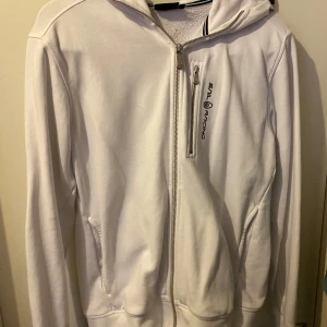 Vit hoodie från Sail Racing - Säljer en snygg vit hoodie från Sail Racing i bra skick. Den har en dragkedja framtill och en liten logga på bröstet. Perfekt för vår och höst, med långa ärmar och en skön passform. Passar både till vardags och lättare träning.