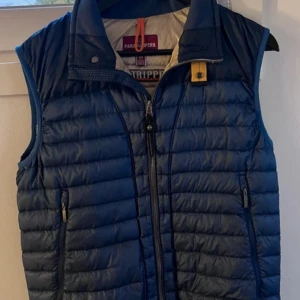Blå dunväst från Parajumpers - Säljer en snygg blå dunväst från Parajumpers i mycket bra skick. Västen har en dragkedja framtill och praktiska fickor med dragkedjor. Perfekt för höst och vår när du vill hålla dig varm men ändå se stilren ut. Passar både till vardags och lite finare tillfällen.