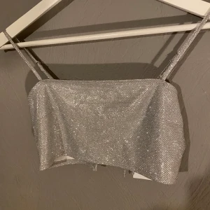 Glittrig silver tubtopp - Säljer en superfin glittrig silver tubtopp med smala axelband. Perfekt för festliga tillfällen! Toppen har en snygg knytning i ryggen för extra detalj. Den är i nytt skick och redo att glänsa på nästa party! ✨(PM OM DU VILL HA FLER BILDER)
