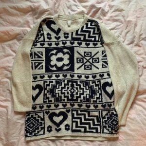 Beige och svart stickad mönstrad tröja - Säljer en superfin beige stickad tröja med svart mönster. Den har långa ärmar och är perfekt för höst och vinter. Mönstret är unikt med hjärtan och geometriska former. Materialet är en blandning av bomull och akryl, vilket gör den både varm och bekväm. Perfekt för att mysa i hemma eller för en casual dag ute. Jag bär vanligtvis xs. Tröjan passar många storlekar, skull he säga från xs-l beroende på hur man vill att den ska sitta.🥰