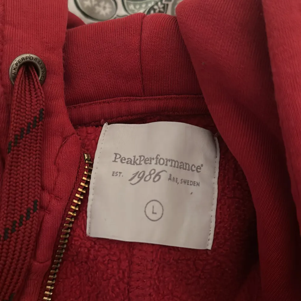 Säljer en snygg röd hoodie från Peak Performance med dragkedja och justerbar huva. Den har en cool '86' design på bröstet och är perfekt för både vardag och chill. Superbekväm och i bra skick!. Neuletakit & Villapaidat.