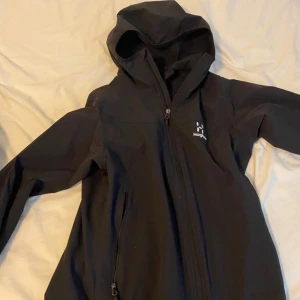 Svart vindjacka från Haglöfs - Säljer en svart vindjacka från Haglöfs i mycket bra skick. Jackan har en dragkedja framtill och en praktisk huva. Perfekt för höst och vår, och den är långärmad för extra skydd mot vinden. Passar bra till både vardag och lättare utomhusaktiviteter.