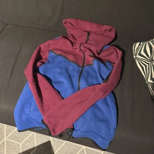 Nike tech zipup - Säljer en snygg nike tech i blått och vinrött med dragkedja. Perfekt för höst och vår, med långa ärmar och en bekväm passform. Den är i bra skick och passar både till vardags och träning.