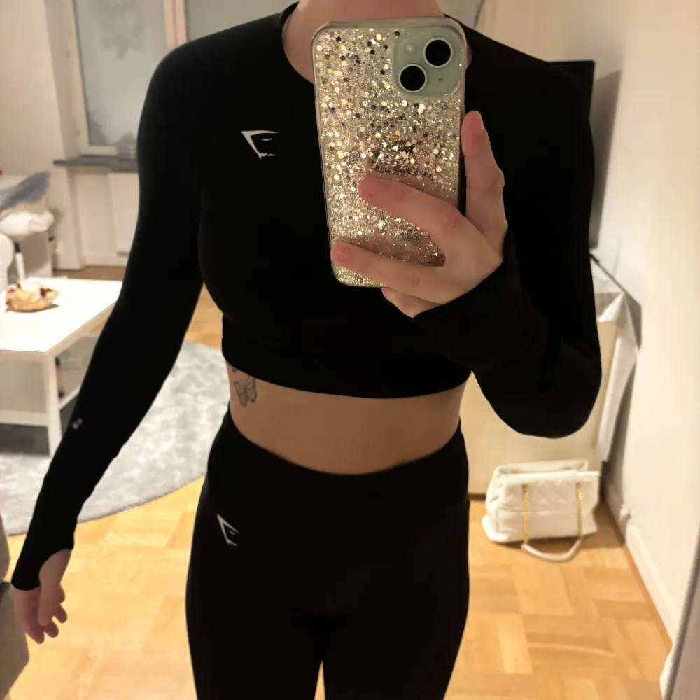 Säljer en svart croppad träningstopp från Gymshark i mycket bra skick. Toppen är tight och har långa ärmar, perfekt för gymmet eller löprundan. Den är gjord i ett stretchigt material som andas bra. Snygg och funktionell för alla träningspass!. Toppar.