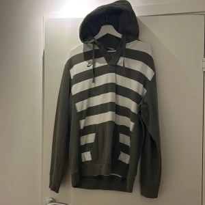 Randig hoodie från Nike - Säljer en grå och vit randig hoodie från Nike med texten 'Eugene, OR./USA' på baksidan. Hoodien har en klassisk design med långa ärmar och en bekväm huva med snörning. Perfekt för en avslappnad stil.