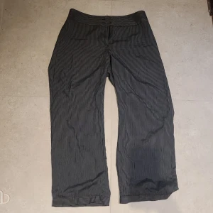Kostymbyxor - Svart/märkgrå randiga kostymbyxor från Almia i strlk 46 (L/XL). Jättesnygg passform och sköna med flowy känsla. En knapp saknas som jag syr på vid köp :)