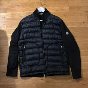 Marinblå moncler cardigan  - Snygg svart jacka från Moncler med quiltad framsida och stickade ärmar. Jackan har en dragkedja framtill och två praktiska fickor med dragkedjor. Perfekt för kyligare dagar, vet dock inte om den är äkta men kan tänka mig gå ner i pris vid en snabb affär 