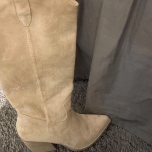 Beige mockastövlar - Snygga beige stövlar i mocka med en stilren design. De har en spetsig tå och en stabil klack som ger en elegant look. Perfekta för både vardag och festliga tillfällen. Jag säljer dom för att jag har så många skor och dom kommer just nu inte till användning, hör av er vid frågor eller liknande🥰💓