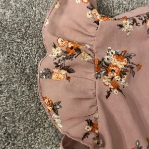 Blus💕 - Charmig blus i en ljus rosa ton med blommigt mönster i orange, vitt och grönt. Klänningen har volangdetaljer vid ärmarna och en rund halsringning. Perfekt för en somrig look! Jag skulle säga att storleken passar xs💕