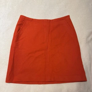 Orange ull kjol från Marc O'Polo - Snygg orange kjol från Marc O'Polo i italienskt tyg. Kjolen har en klassisk A-linjeform och är perfekt för att ge en färgklick till din outfit. Den har en diskret dragkedja i sidan för enkel på- och avtagning. Materialet är i ull.