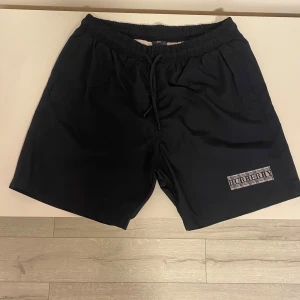 Svarta shorts från Burberry - Snygga svarta shorts från Burberry med elastisk midja och snörning. Har ett klassiskt Burberry-mönster på loggan. Perfekta för en stilren look.  Fick dem av min kusin i somras men dem är för små och kan inte garantera äktenskap 
