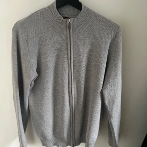 Grå stickad kofta från Stenströms - Säljer en stilren grå stickad kofta från Stenströms med dragkedja framtill. Perfekt för kyliga dagar och enkel att matcha med olika outfits. Koftan har långa ärmar och en ribbad krage för extra komfort. 10/10 skick inga syn av slitage. 