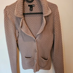 Beige stickad kofta från H&M - Mysig beige stickad kofta från H&M med knappar framtill och två fickor. Perfekt för kyliga dagar med sin klassiska design och bekväma passform.