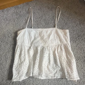 Vit ärmlös topp med spetsdetaljer - Söt vit topp med tunna axelband och vackra spetsdetaljer. Toppen har en luftig passform och är perfekt för varma sommardagar. Den har en smockad rygg för extra komfort och stil. Passar xs å s!! Kolla in min Vinted om du vill köpa flera varor på en gång för lite rabatt, astrid450 💞