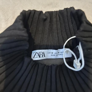 Svart ribbad klänning från Zara - Snygg svart klänning från Zapa med ribbad design och transparenta detaljer. Klänningen har långa ärmar och en hög krage, vilket ger en elegant look. Perfekt för en stilren outfit.