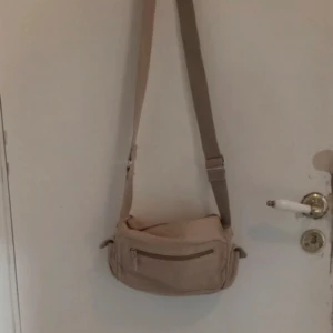Beige axelväska med dragkedja - Säljer en praktisk beige axelväska med justerbar rem och flera dragkedjefickor. Perfekt för att hålla ordning på dina saker när du är på språng.