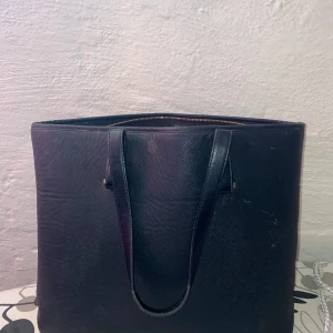 Svart axelväska med dragkedja - Snygg och rymlig svart axelväska i skinn med praktisk dragkedja upptill. Perfekt för att bära med sig allt man behöver under dagen. Stilren design som passar till många olika outfits.