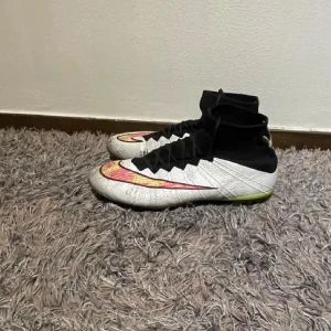 Nike Superfly 4 - Snygga fotbollsskor från Nike i grått och svart med färgglada detaljer. Skorna har snörning och en hög ankelkrage för extra stöd. Perfekta för fotbollsplanen med sin slitstarka design och greppvänliga dobbar.
