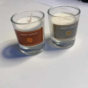 Doftljus Suede Vanilla och Sweet Jasmine från Rituals - Två eleganta doftljus från Rituals Private Collection. Suede Vanilla har en varm och mjuk vaniljdoft, medan Sweet Jasmine erbjuder en söt och blommig jasminarom. Båda ljusen är i genomskinliga glasbehållare med stilrena etiketter i brunt och grönt.