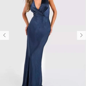 Mörkblå långklänning med v-ringning - Elegant mörkblå långklänning med djup v-ringning och omlott-design. Perfekt för festliga tillfällen. Sitter intr likadant på mig vid brösten då jag använde mig av en säkerhetsnål ( inte lämnat någon slags av märke på klänningen) 