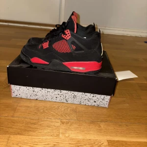 Svarta och röda Nike Air Jordans - Säljer ett par klassiska Nike Air Jordans i svart och rött. Skorna har snörning och den ikoniska Jumpman-loggan på tungan och hälen. Perfekta för sneakerheads som vill ha en tidlös stil.
