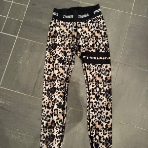 Leopardmönstrade leggings från Stronger - Snygga leopardmönstrade leggings från Stronger med elastisk midja och svarta detaljer. Perfekta för träning eller en avslappnad dag. De har en tight passform som ger bra stöd och komfort.