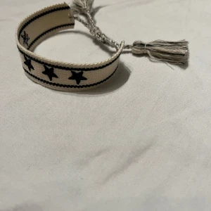 Vit armband med stjärnor - Snyggt beige armband med svarta stjärnor och justerbar. Perfekt accessoar för en unik stil. Ger en fin liten extra touch i din outfit