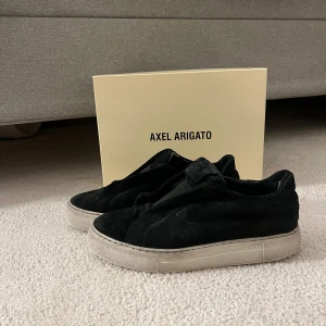 Svarta sneakers från Axel Arigato - Snygga svarta sneakers från Axel Arigato i mocka med en stilren design. Skorna har en vit sula som ger en fin kontrast till det svarta. Perfekta för en avslappnad och trendig look.