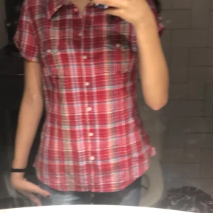 Röd rutig skjorta från L.O.G.G. - Säljer en snygg röd rutig skjorta från L.O.G.G. med korta ärmar och knappar framtill. Skjortan har två bröstfickor och är perfekt för en avslappnad stil. Tillverkad i bomull för en bekväm känsla.