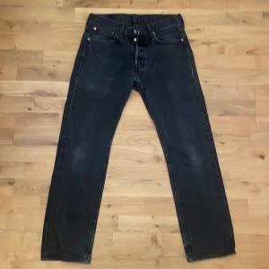 Svarta Levi's 501 jeans W31 L32 - Säljer ett par klassiska svarta Levi's 501 jeans. De har en rak passform och är tillverkade i slitstarkt denim. Perfekta för en stilren look med fem fickor och knappgylf. Skick 10/10. Storlek: W31 L32.