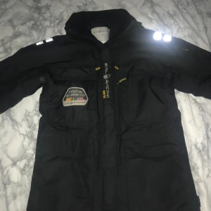 Svart jacka från Sail Racing - Snygg svart jacka från Sail Racing med reflekterande detaljer och flera praktiska fickor. Jackan har en hög krage och är tillverkad i Gore-Tex-material för extra skydd mot väder och vind. Perfekt för kyliga dagar. Obs luvan är tyvär borta köpte den för 6 tusen 