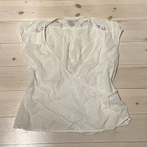 Vit omlottblus  - Säljer en söt vit omlottblus med spetsdetaljer vid ärmslut och hals och silver detaljer. Blusen har korta ärmar och ett knytband i midjan för en fin passform. 💕