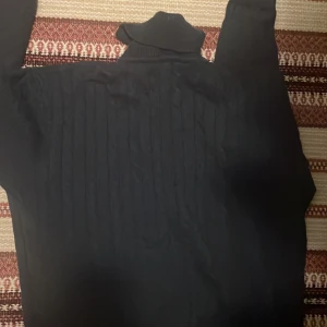 Svart polotröja från John Henric - Säljer en stilren svart polotröja från John Henric. Tröjan har en klassisk design med ribbade detaljer vid kragen och ärmsluten. Perfekt för kyligare dagar och kan enkelt matchas med olika outfits.