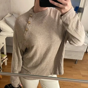 Beige tröja med knappar - Säljer en stilren beige tröja med långa ärmar och dekorativa knappar vid halsen. Perfekt för en avslappnad look💋