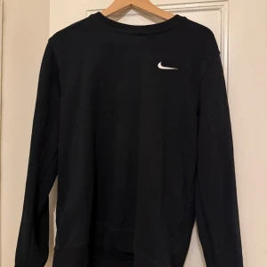 Sweatshirt  Nike - Säljer en svart långärmad tröja från Nike med en vit logga på bröstet. Perfekt för en sportig och avslappnad stil. Tröjan är enkel och stilren, idealisk för vardagsbruk.