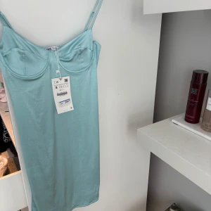 Ljusblå klänning med smala axelband - Snygg ljusblå klänning med smala axelband och bygel för extra stöd. Perfekt för varma dagar eller sommarfester. Klänningen har en elegant och enkel design som framhäver figuren. Aldrig använd pga fel storlek. Den har en super fint silkes material!