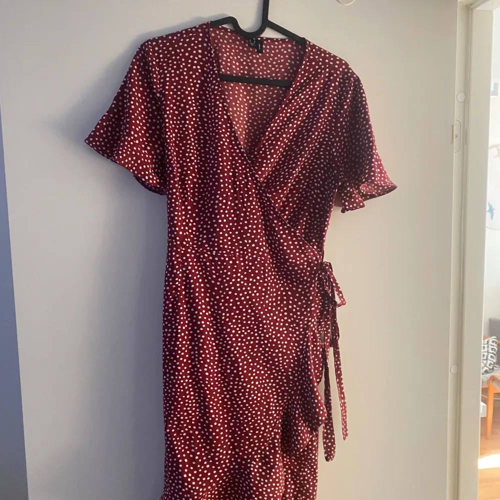 Vero Moda (Henna Wrap Frill Dress) omlottklänning röd med vita prickar. En söt klänning med snörning i sidan i ett skönt och luftigt material. Bra skick i storlek 38❤️. Klänningar.