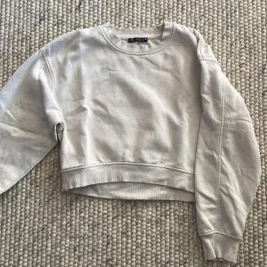 Beige croppad sweatshirt från Zara - Säljer en superfin naturvit croppad sweatshirt från Zara. Den är perfekt för en avslappnad look och har långa ärmar. Materialet är mjukt och skönt, perfekt för höst och vår. Passar bra till jeans eller kjol 