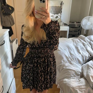 Svart kort klänning med blommor - Säljer denna SUPERSNYGGA klänningen från NA-KD. Asså den formar kroppen så fint med resoren i midjan och sen den lite puffiga kjolen som gör att du får så fin figur!😍Inga tecken på användning. Slutsåld på nakd och nypriset ligger på 450 kr.