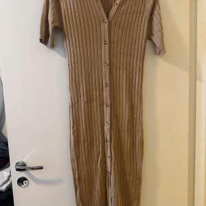 Beige ribbad klänning från Rut & Circle - Säljer en superfin beige ribbad klänning från Rut & Circle. Den har en v-ringad design med knappar hela vägen ner och trekvartsärmar. Perfekt för både vardag och fest! 