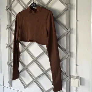 Tröja H&M - En brun, figursydd topp med långa ärmar och hög hals. Toppen är i en ribbstickad struktur och har en något kortare längd. Den är i väldigt fint skick och använd max 2 gånger!