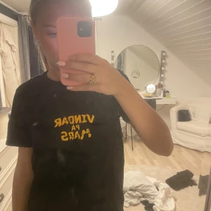Svart t-shirt med tryck - Säljer en svart t-shirt i storlek S med  tryck på både fram- och baksidan, framsidan står det 'Vingar på Mars' i gult och på baksidan finns en stor gul planet (mars). Hov1 merch från ”Vindar på Mars”! Är hov1 loggan på höger armen också 😇🥰