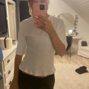 Vit topp med smockdetaljer - Säljer en superfin vit topp med smockdetaljer som ger en snygg och bekväm passform. Toppen har trekvartsärmar och en söt volangkant längst ner. Perfekt för både vardag och fest! Det är den Populära tröjan från HM och knappt använd i M