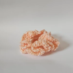 Persikofärgad stickad scrunchie - En superfin persikofärgad scrunchie som är virkad och perfekt för att ge en söt touch till din frisyr. Den är mjuk och elastisk, vilket gör den bekväm att bära hela dagen. Perfekt accessoar för både vardag och fest!